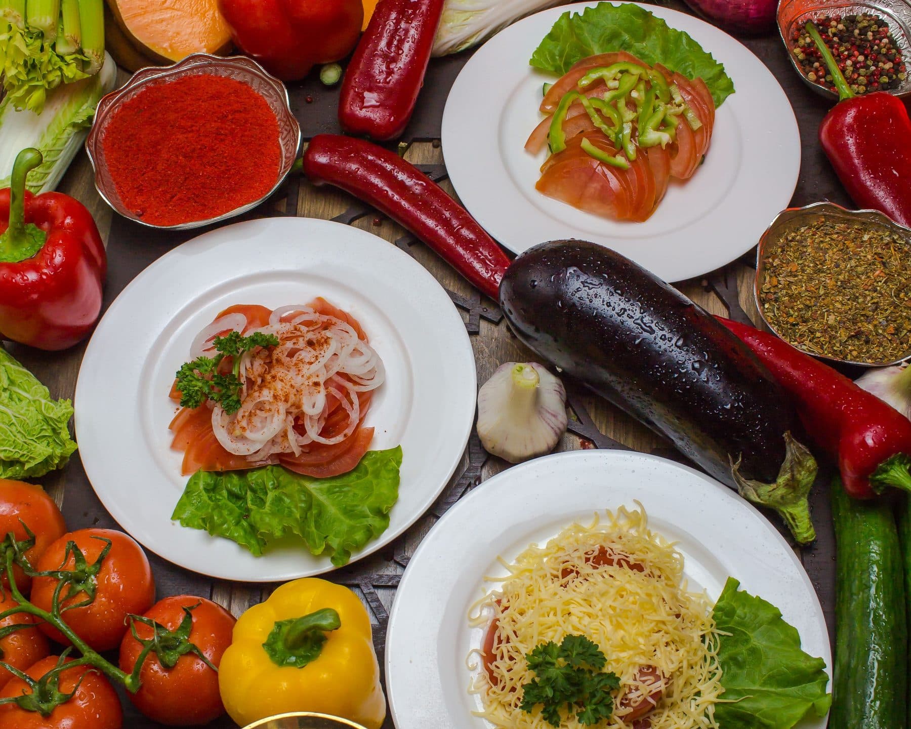 A table seen from above: red peppers and chillies, tomatoes, greens, and three plated dishes
